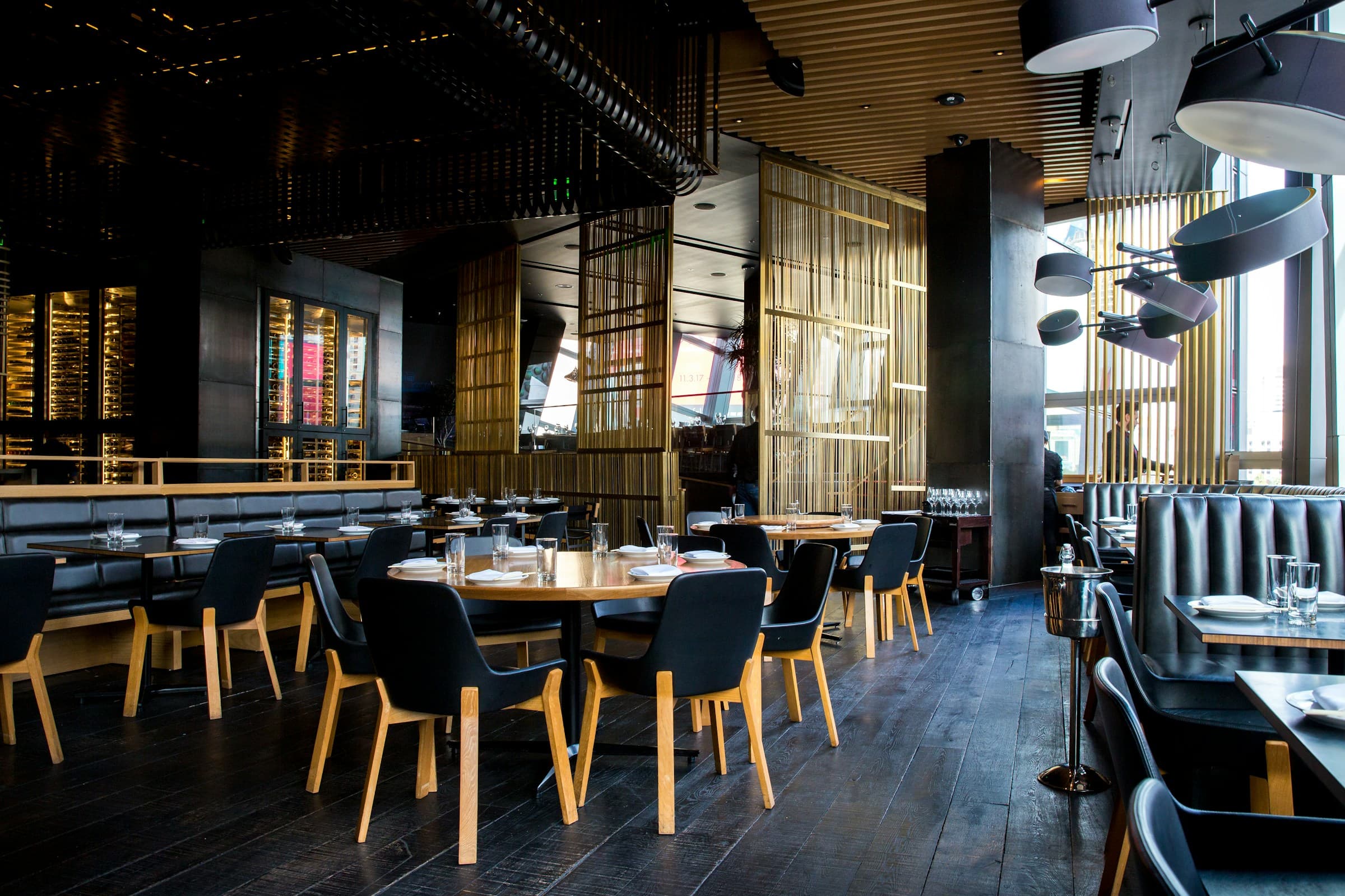 Interior de un restaurante con mesas de madera, tabiques de listones dorados y luz cálida